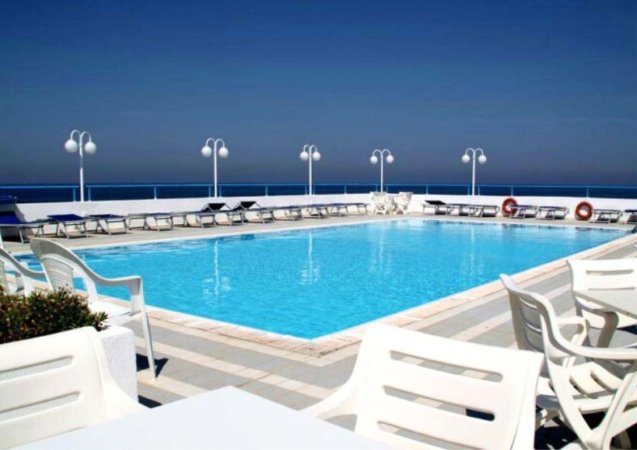 Piscina all'aperto con lettini e vista sul mare.