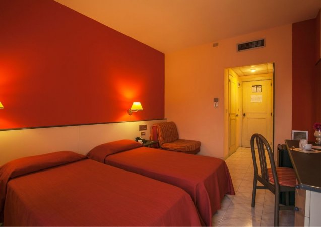 Camera d'hotel con due letti singoli e pareti rosse.