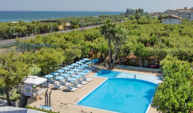 Una piscina con lettini, circondata da alberi.