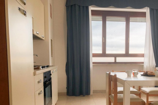 Interno di una cucina con tavolo bianco e tende blu.