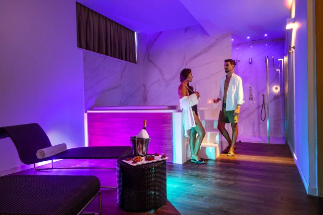 Spa illuminata con due persone e vasca idromassaggio.
