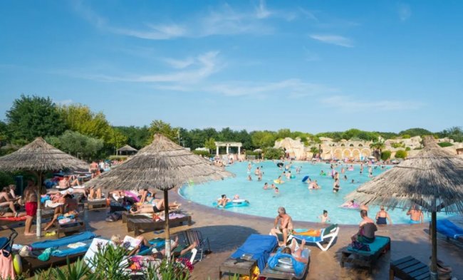 Una grande piscina con molte persone sotto ombrelloni di paglia.