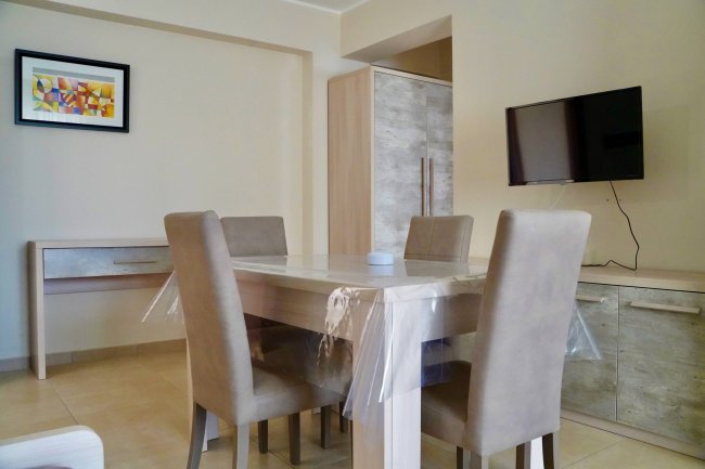 Sala da pranzo con tavolo quadrato e televisore.