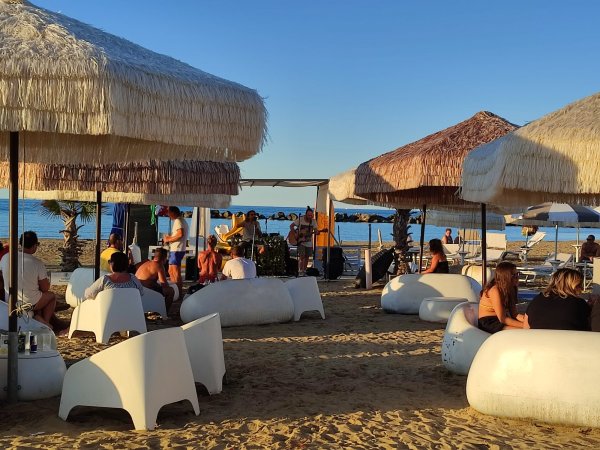 Persone sedute sotto ombrelloni in spiaggia al tramonto.