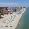 Una spiaggia con ombrelloni e lettini, palazzi e mare tranquillo.
