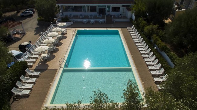 Piscina rettangolare circondata da lettini e ombrelloni bianchi.