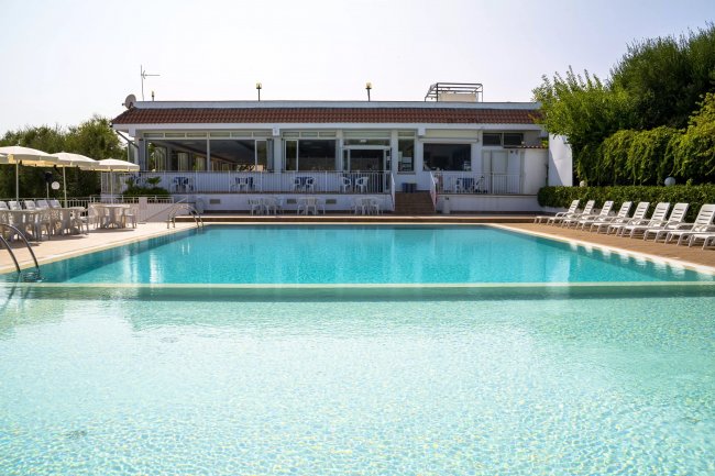 Piscina con sdraio e un edificio sullo sfondo.