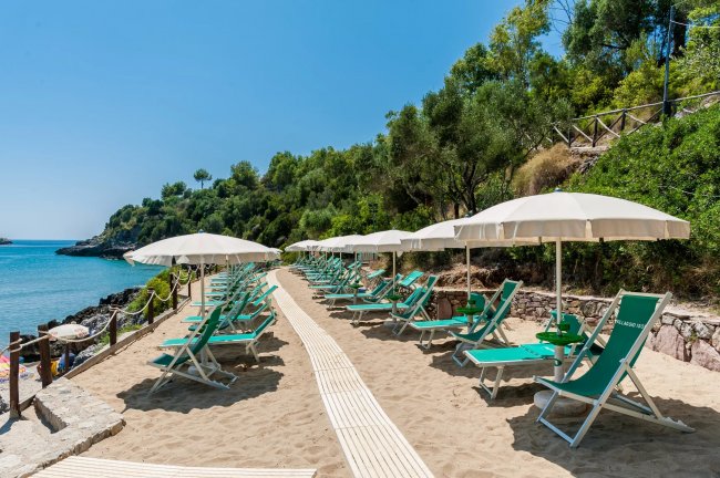 Sentiero di sabbia con sedie a sdraio e ombrelloni.