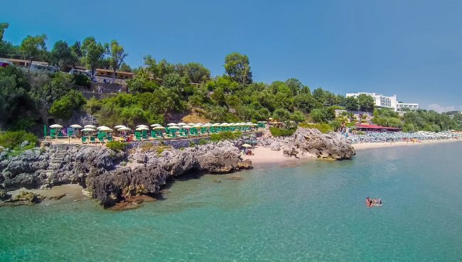 Spiaggia rocciosa con ombrelloni e mare limpido.