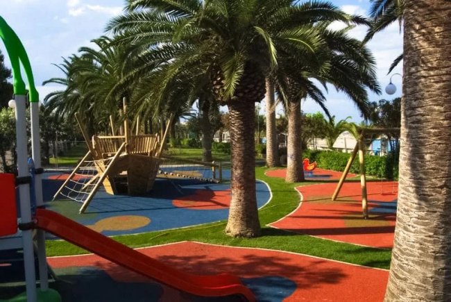 Parco giochi con palme e scivoli colorati.