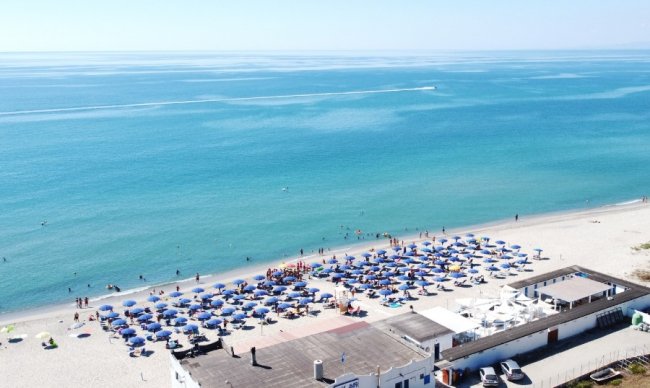 Vista aerea di una spiaggia con ombrelloni blu e bagnanti nel mare.