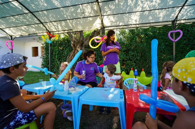 Bambini sotto un tendone giocano con educatori usando palloncini modellabili.