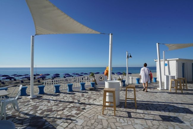 Terrazza con pavimento a mosaico affacciata su una spiaggia con ombrelloni blu.