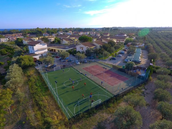 Un campo sportivo con campi da calcetto e tennis, circondato da edifici e verde.