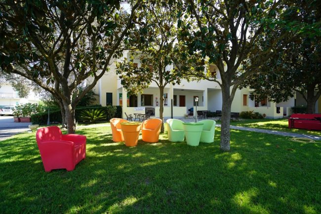 Sedie colorate sotto alberi in un giardino di una struttura residenziale.