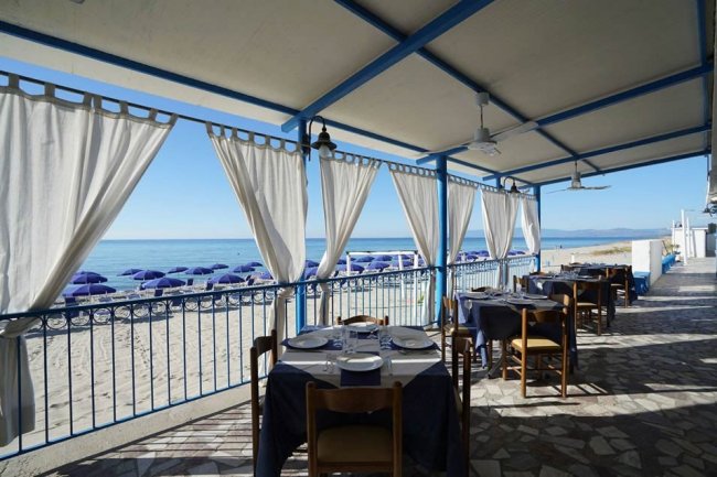 Tavolo apparecchiato su una terrazza vista mare con tende bianche.