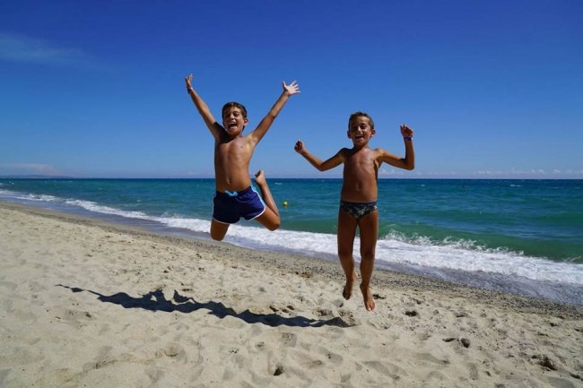 Due bambini felici saltano sulla spiaggia davanti al mare.