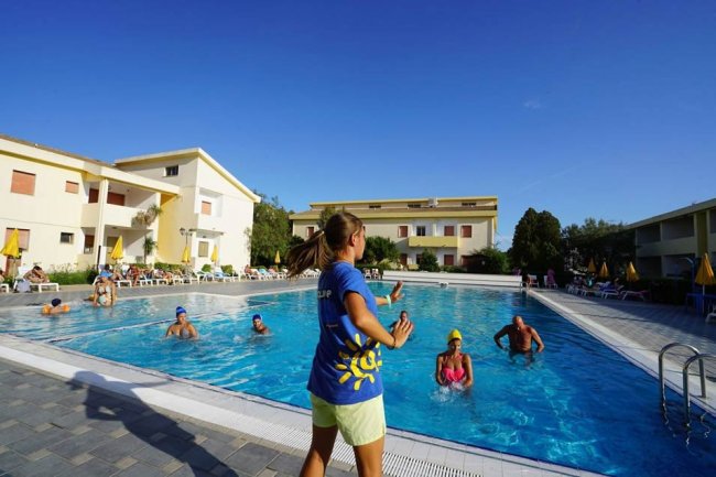 Una persona guida un gruppo in una piscina all'aperto, circondata da edifici gialli.