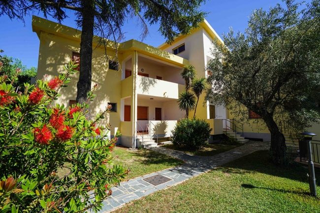 Edificio giallo con giardino esterno e alberi, percorso di pietra.