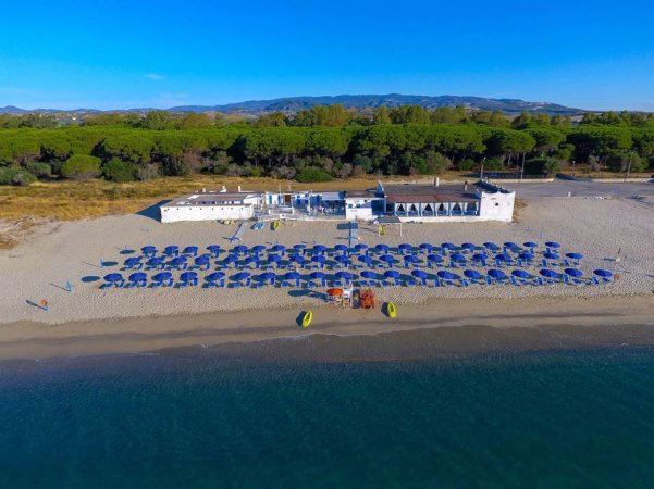 Spiaggia con ombrelloni blu e un edificio bianco, vista dall'alto.